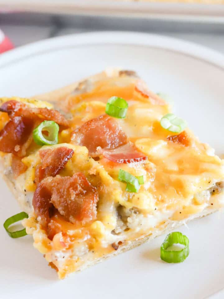 Square of crescent roll breakfast pizza on a white plate with pan in background.