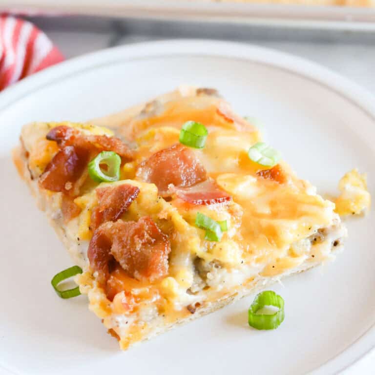 Square of crescent roll breakfast pizza on a white plate with pan in background.