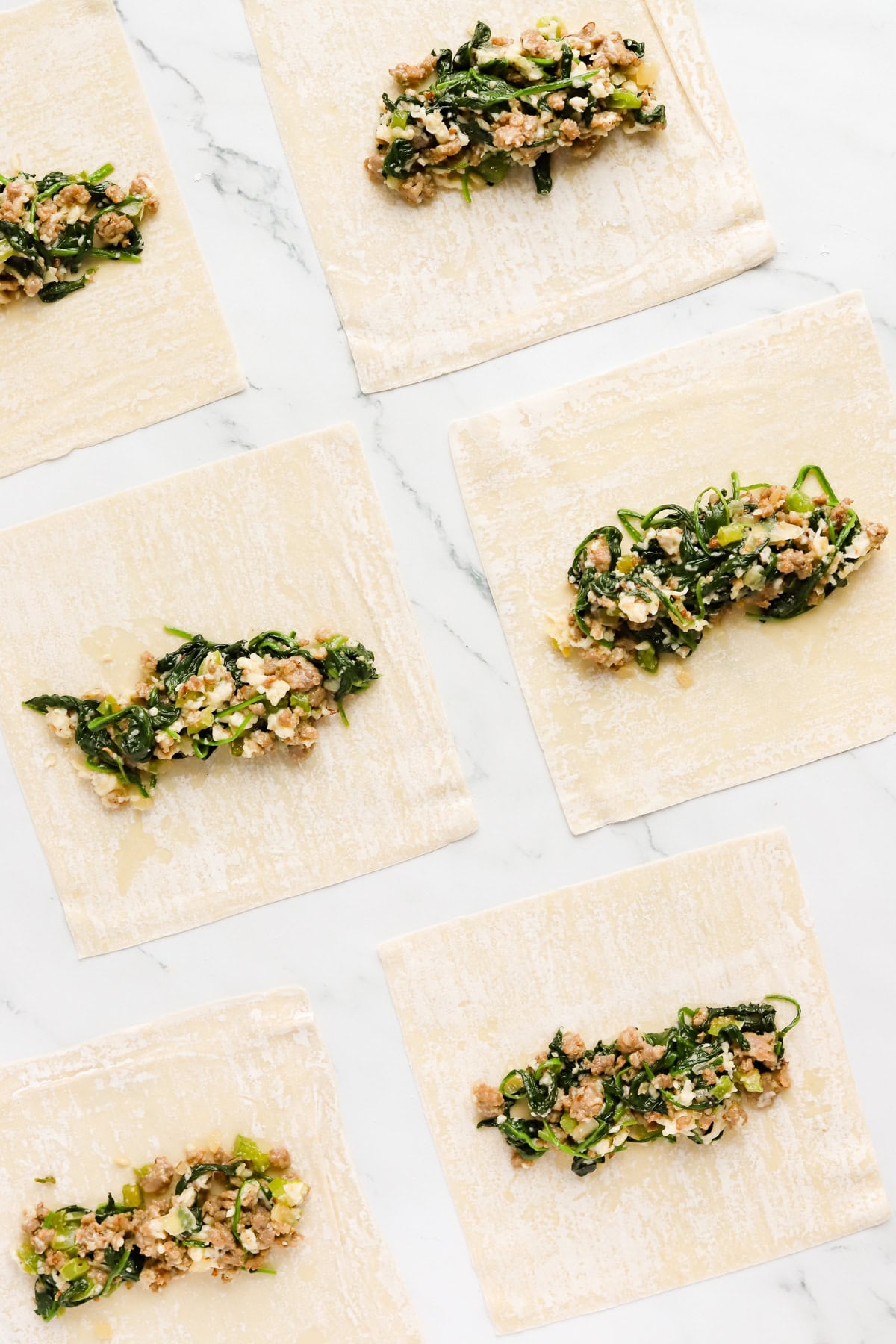 Cooked sausage, spinach and cheese filling laid out in the middle of each egg roll wrapper.