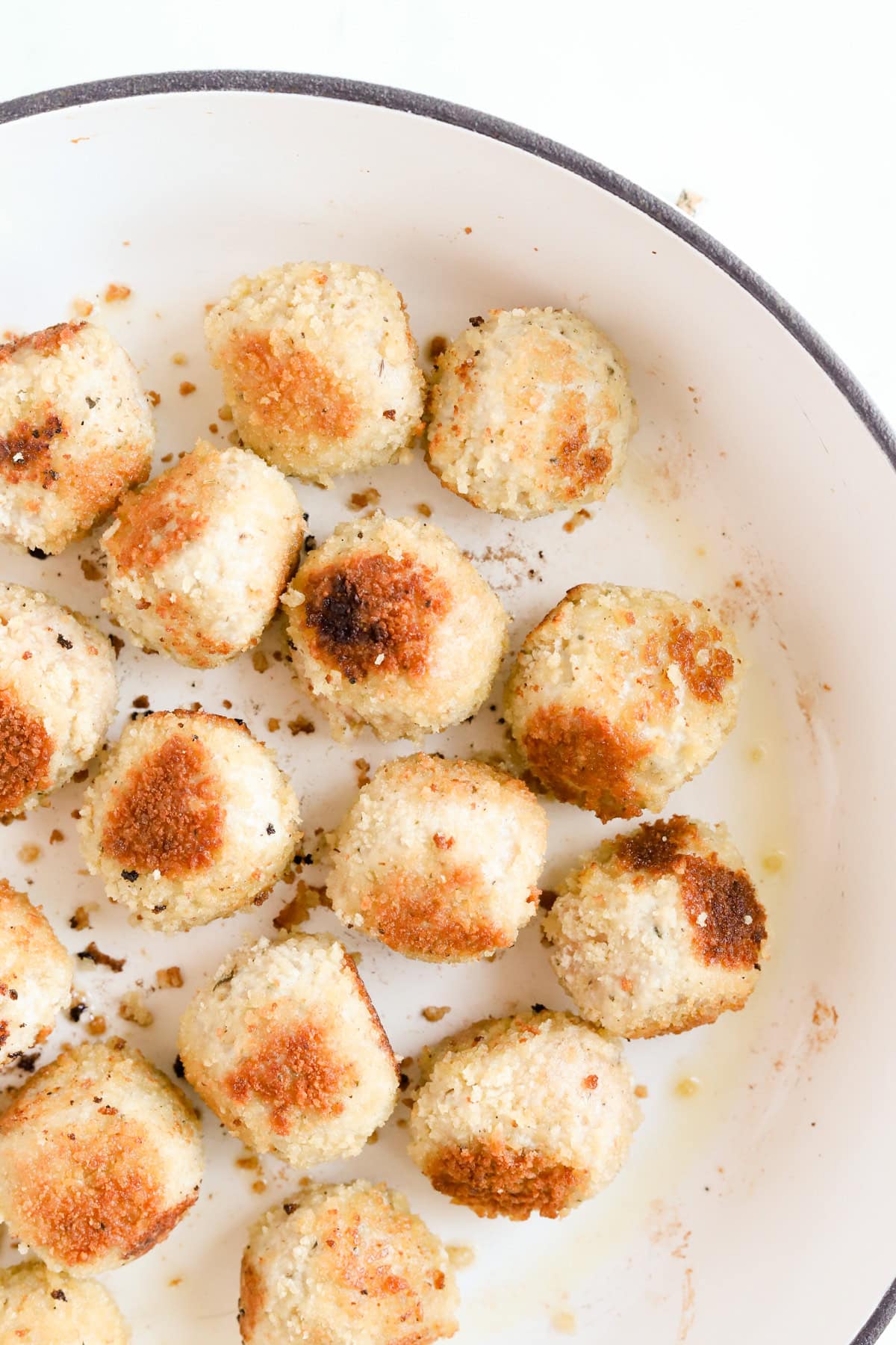Browned chicken meatballs in white skillet.