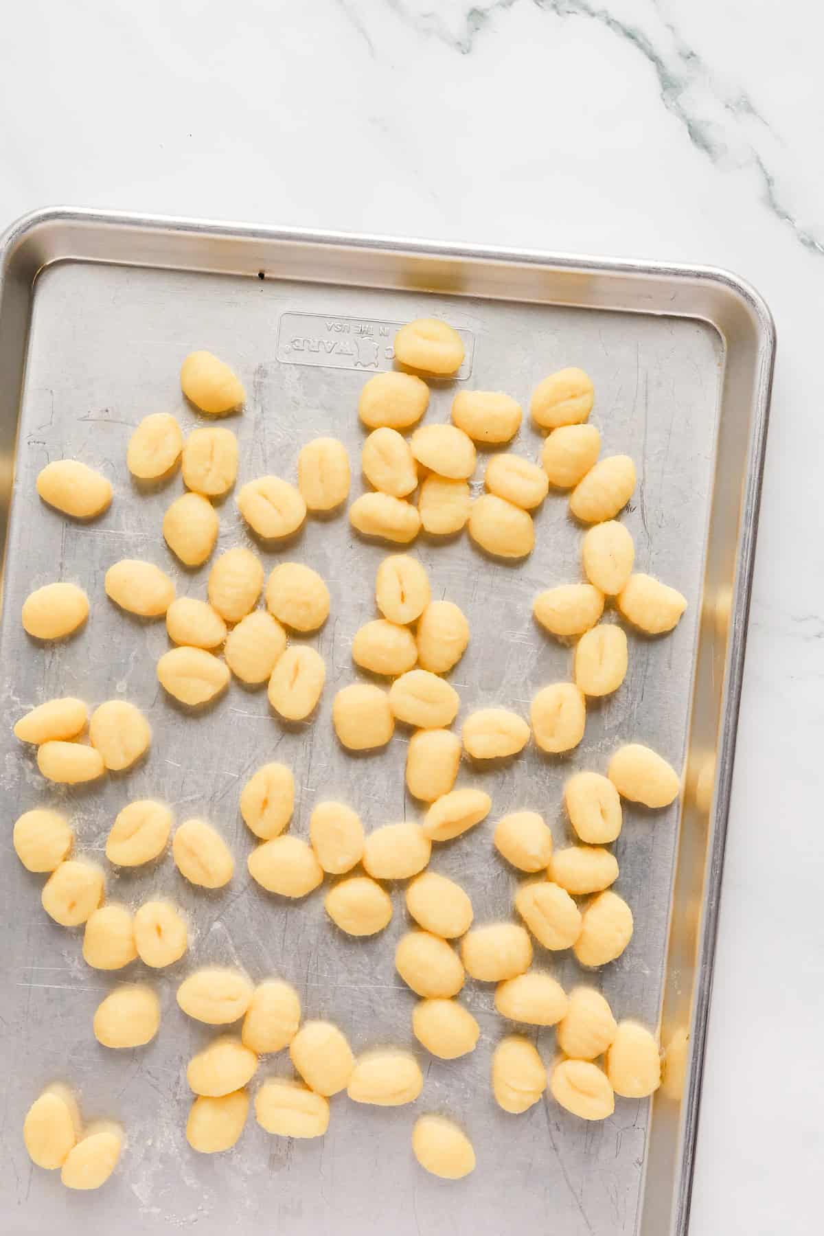 Cooked gnocchi cooling on a sheet pan.