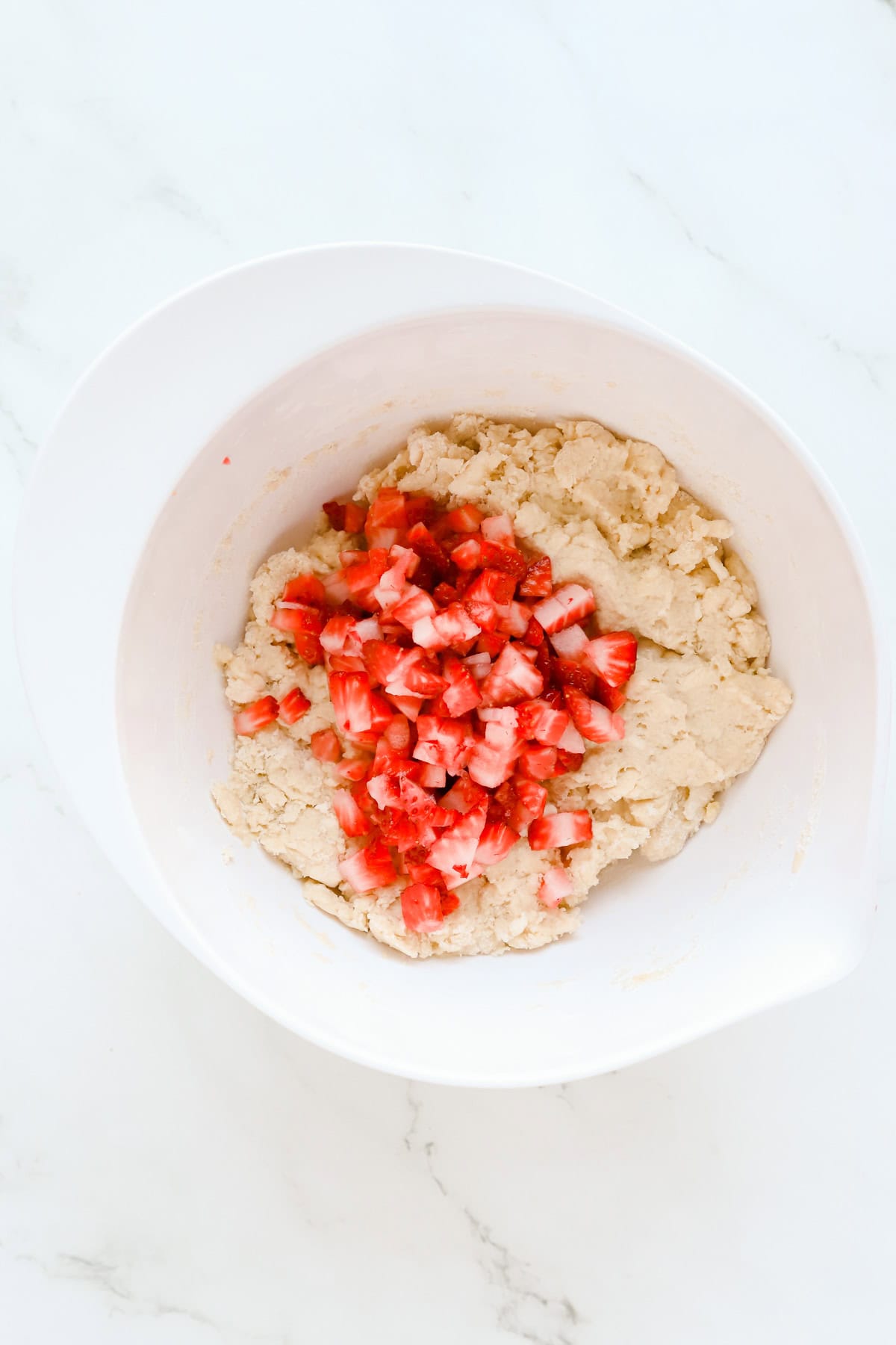 Chopped strawberries in on top of scone batter in a white bowl.