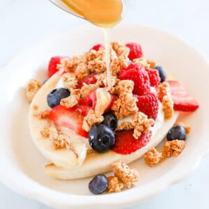 Spoon drizzling honey over breakfast banana split with granola and berries.