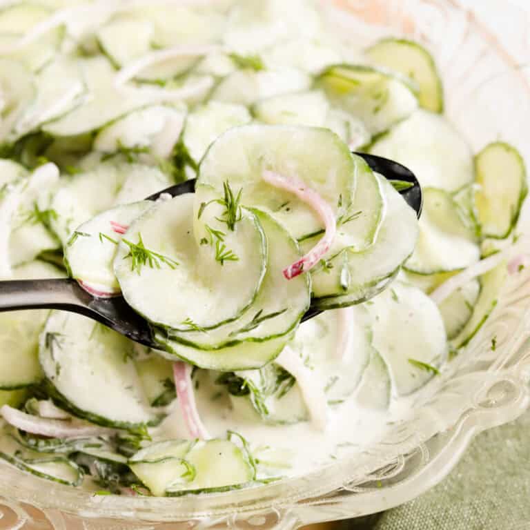 black spoon with a scoop of cucumber dill salad from a glass serving bowl.