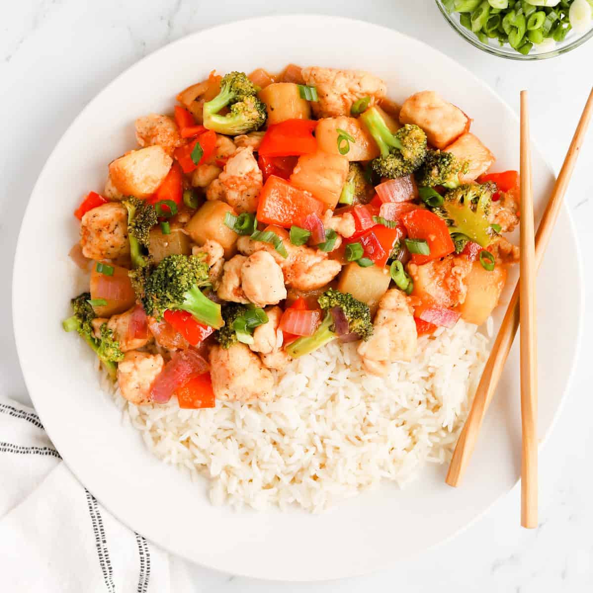Featured image of pineapple chicken stir fry over rice on a white plate with chopsticks