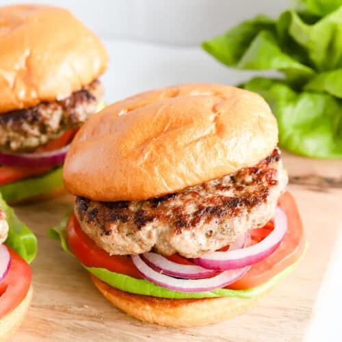 Featured photo of pork burger on buns with lettuce, tomato and red onion.