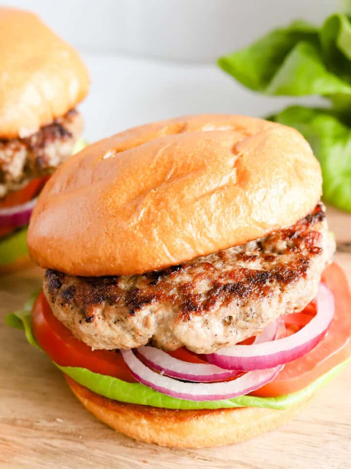 Featured photo of pork burger on buns with lettuce, tomato and red onion.