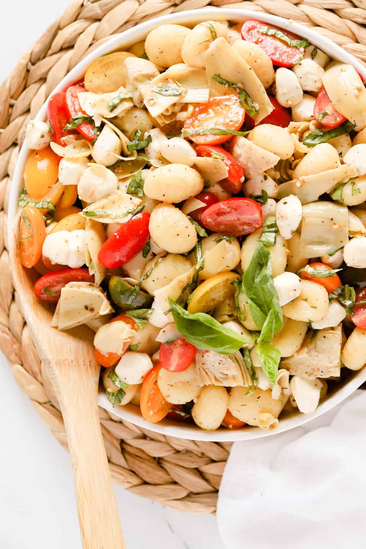 Overhead view of italian gnocchi salad in a white serving bowl on a wicker placemat.