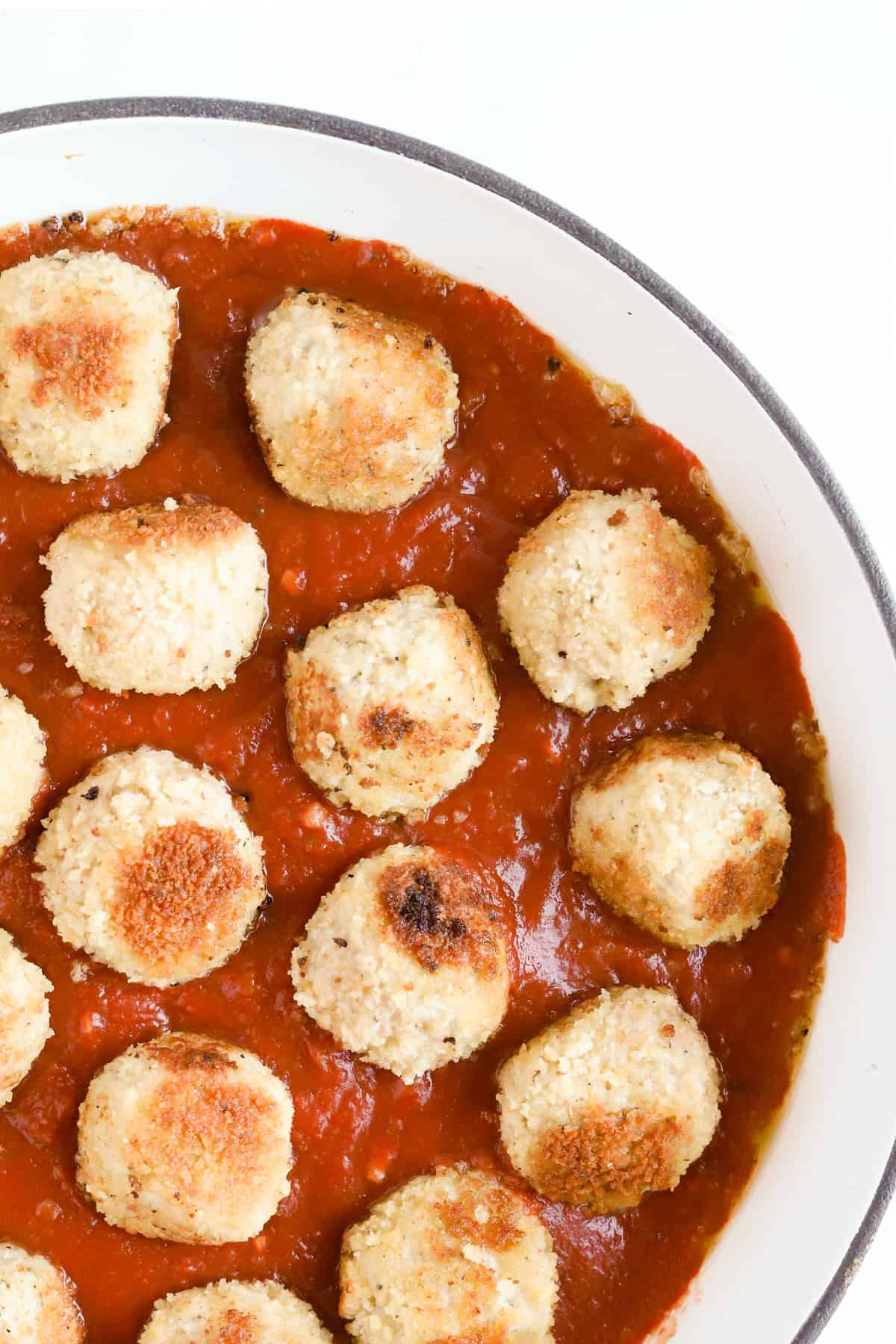 Browned meatballs in marinara sauce in skillet.