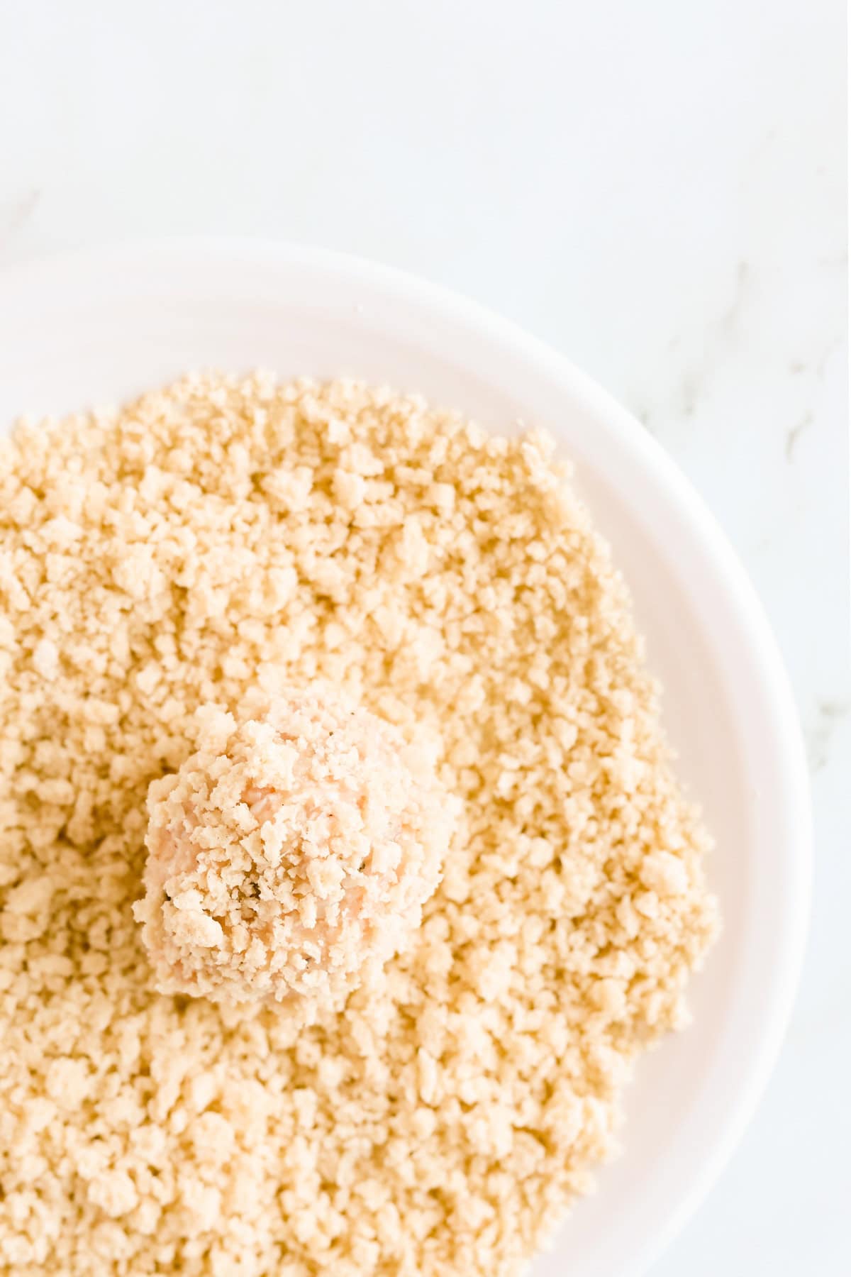 Meatball rolled in panko breadcrumbs on a white plate.