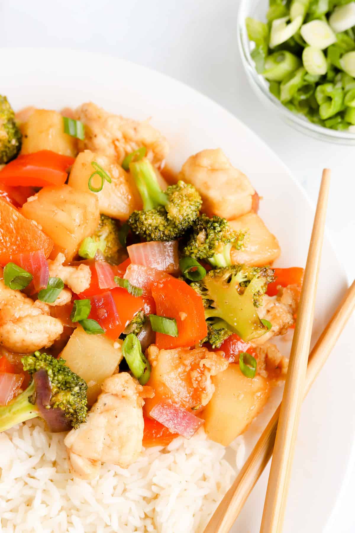 Close up of pineapple chicken stir fry on a white plate with chopsticks and green onions.