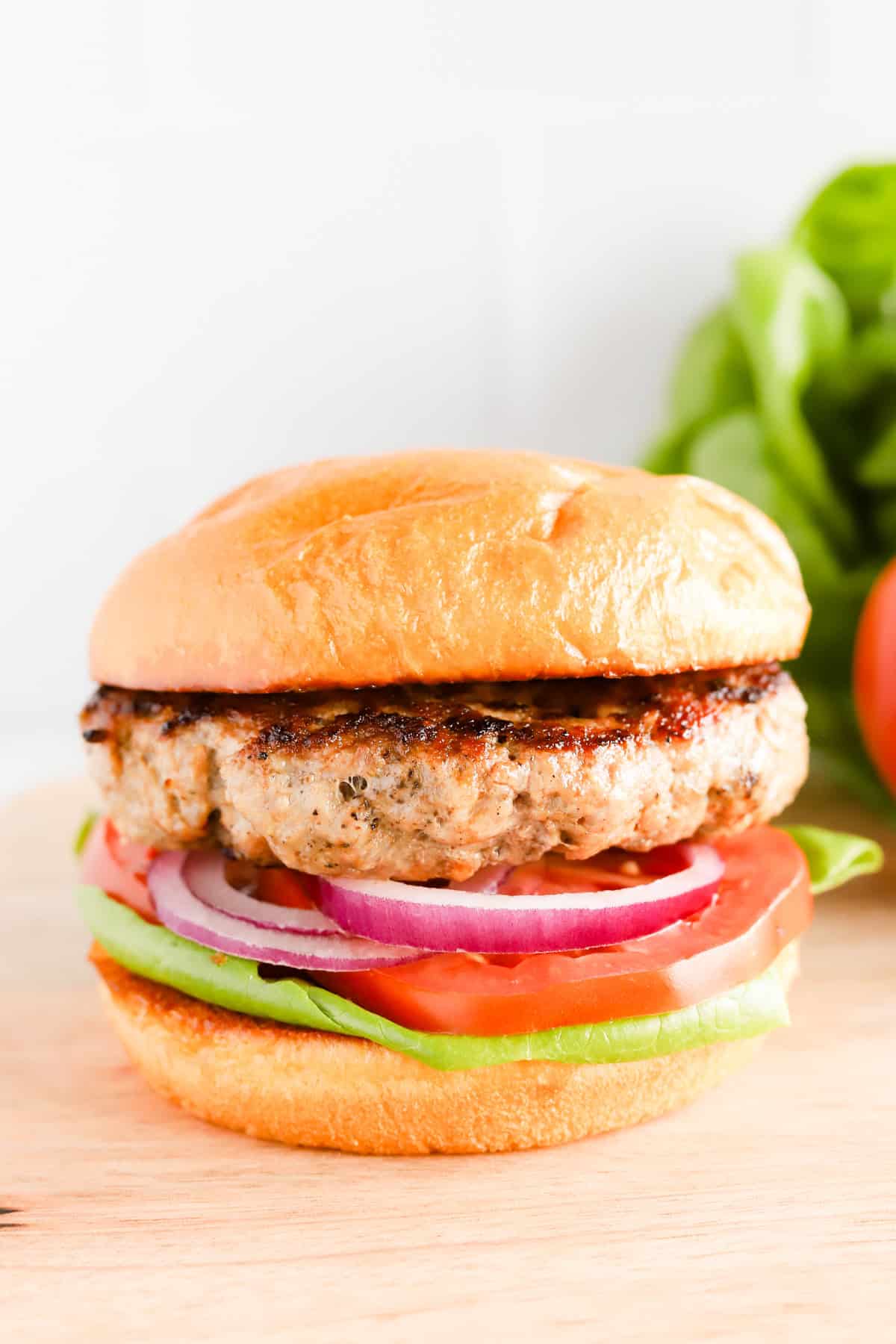 Close up of pork burger on brioche bun with red onion, sliced tomato and lettuce.