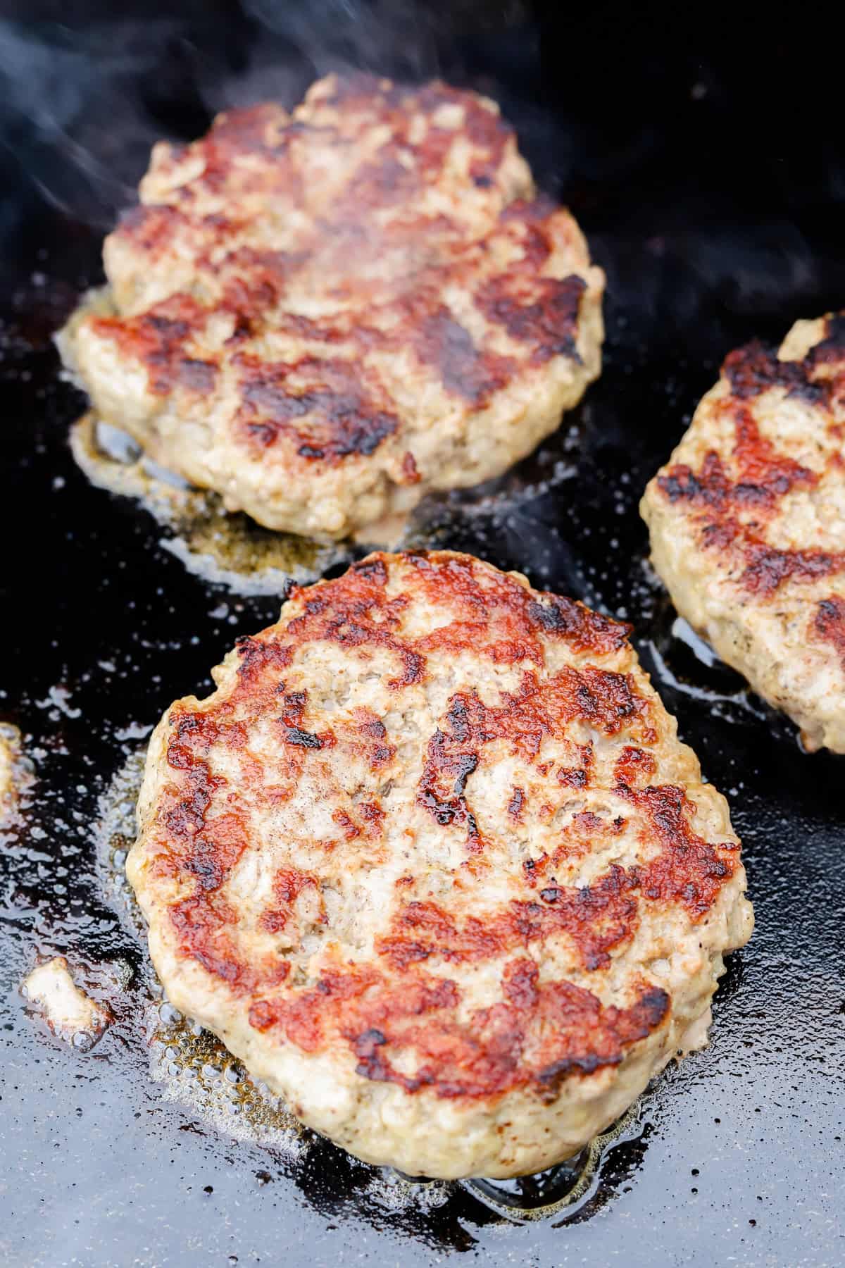 Pork burgers cooking on flattop grill.