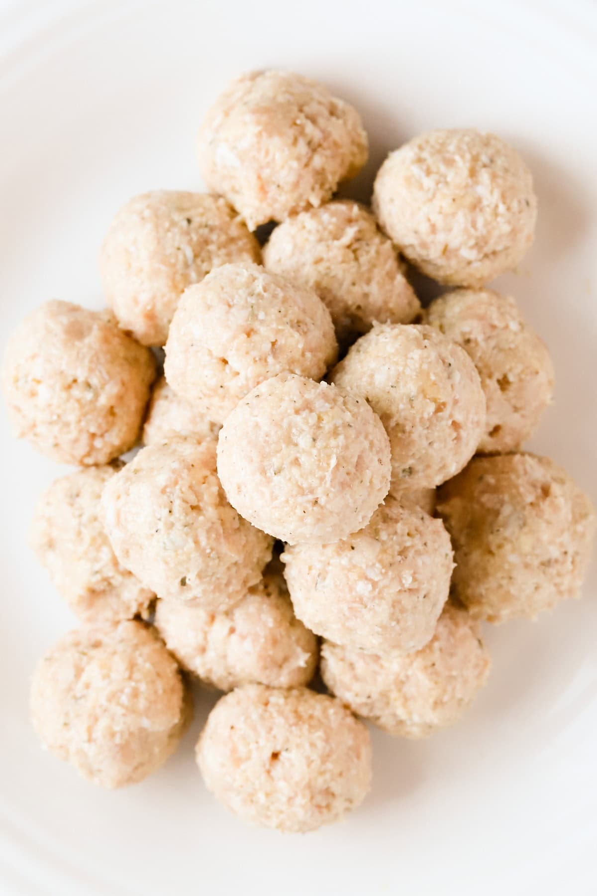 Raw chicken meatballs stacked on a white plate.