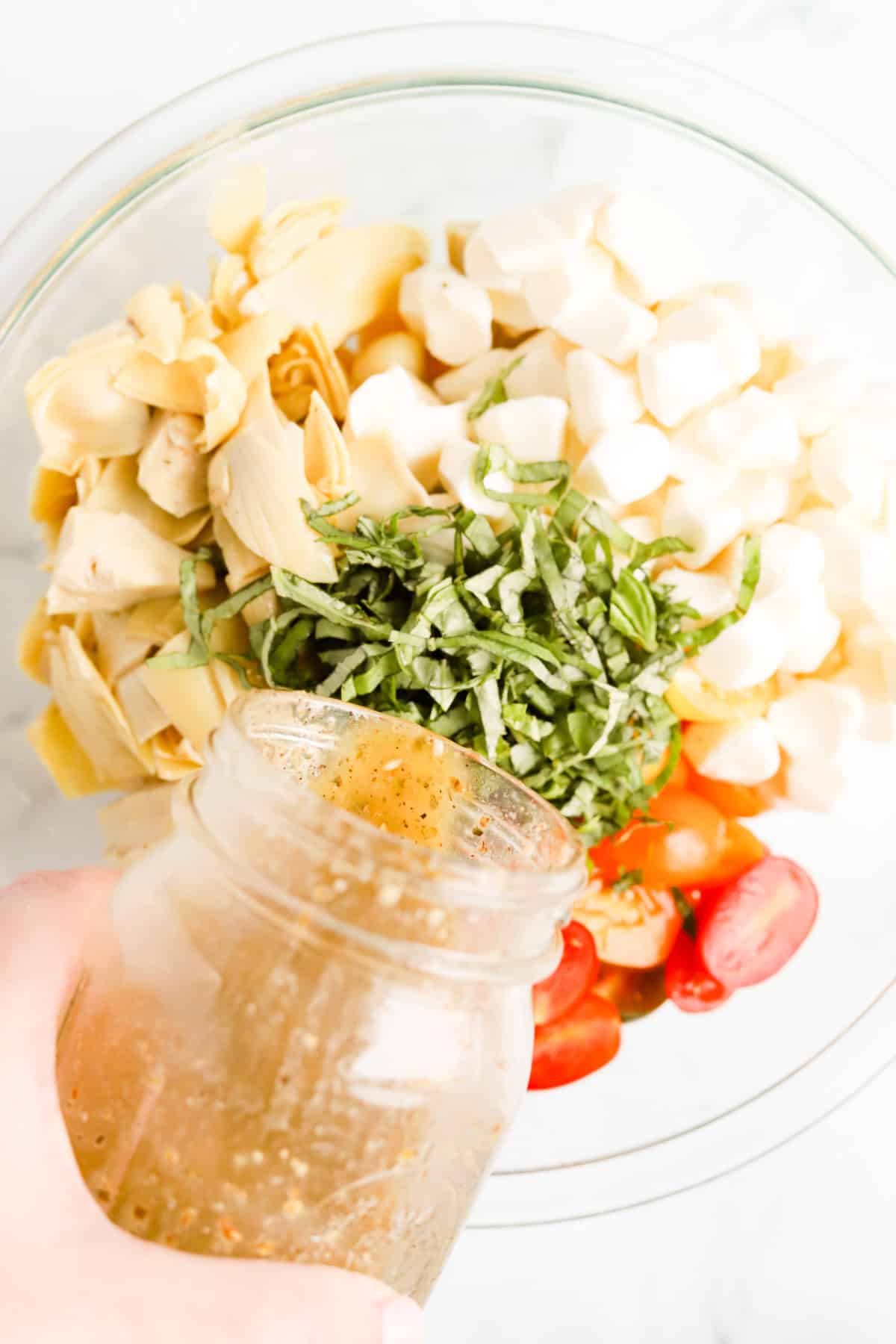 Mason jar of red wine vinaigrette being poured into gnocchi, cheese and veggies.