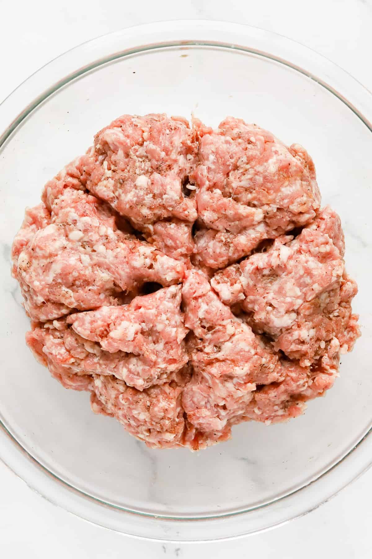 Seasoned pork mixture divided into 6 wedges in a glass bowl.