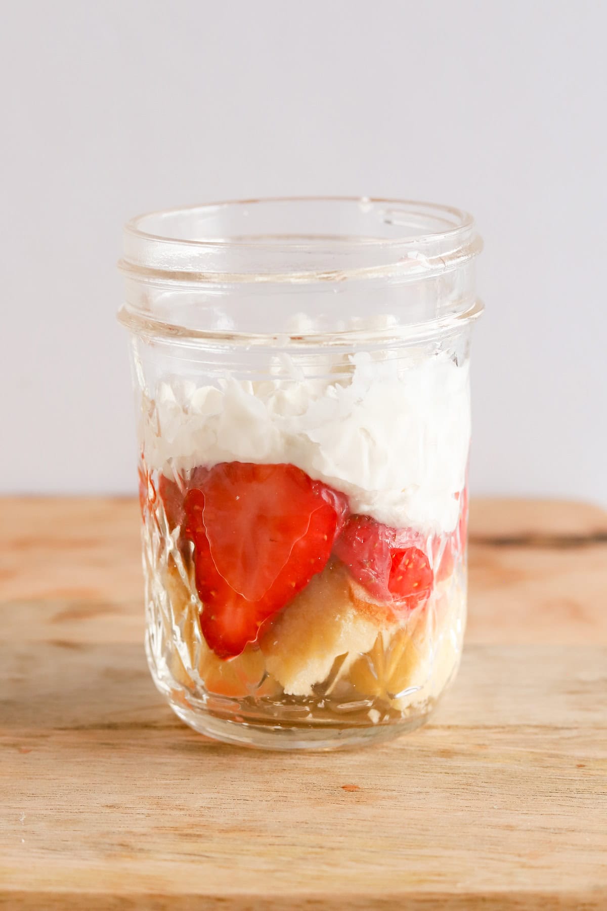 First layers of pound cake, strawberries and whipped cream in mason jar.