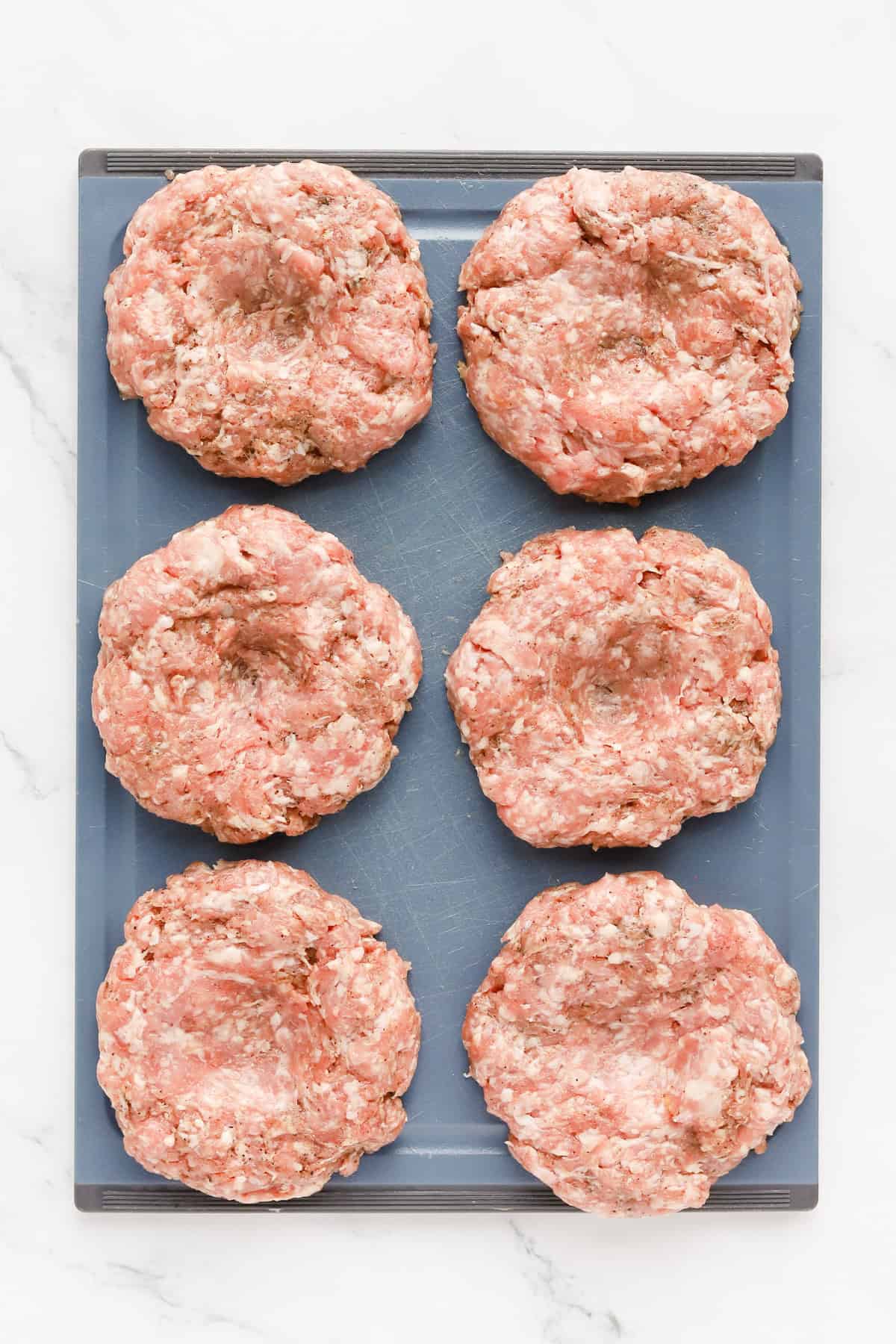 Raw pork patties on a dark gray cutting board.