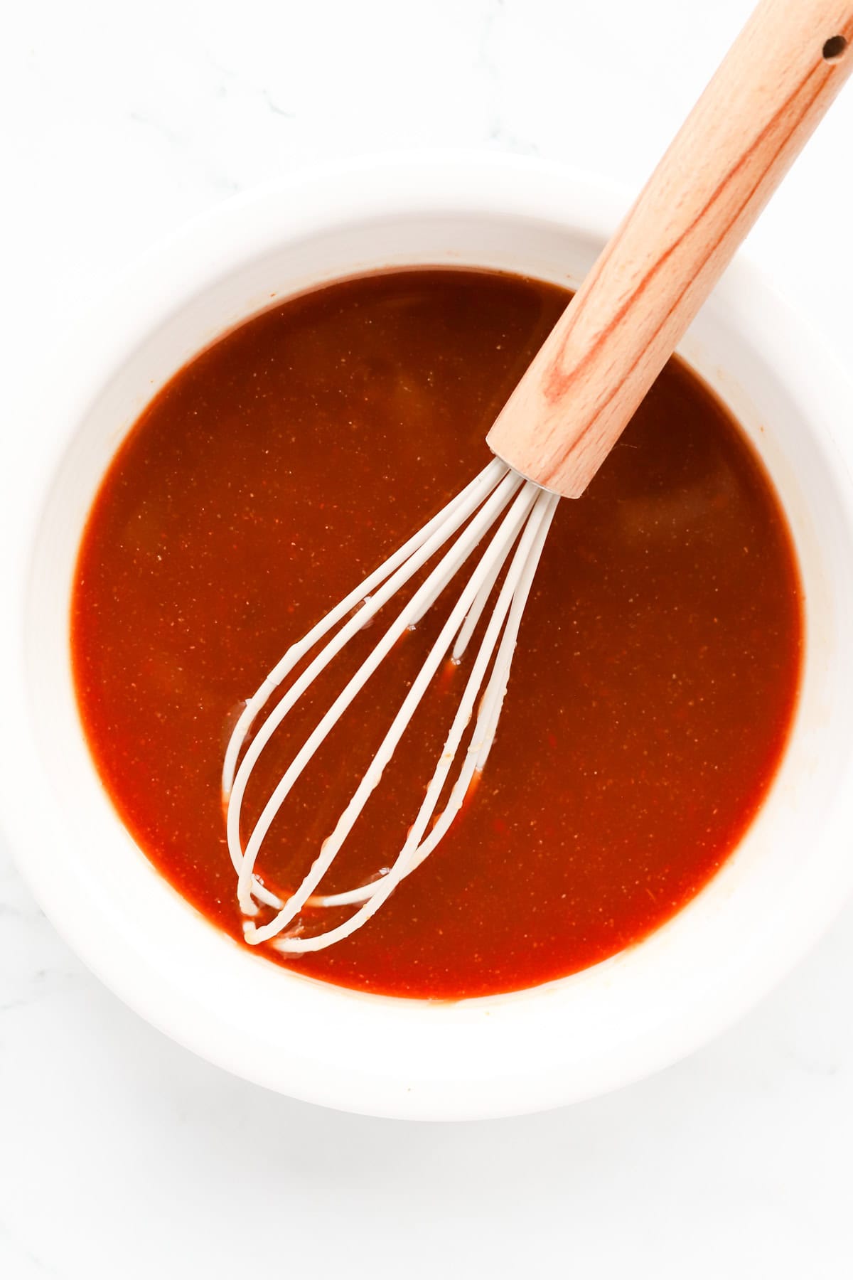 White bowl of homemade sweet and sour sauce with a whisk.