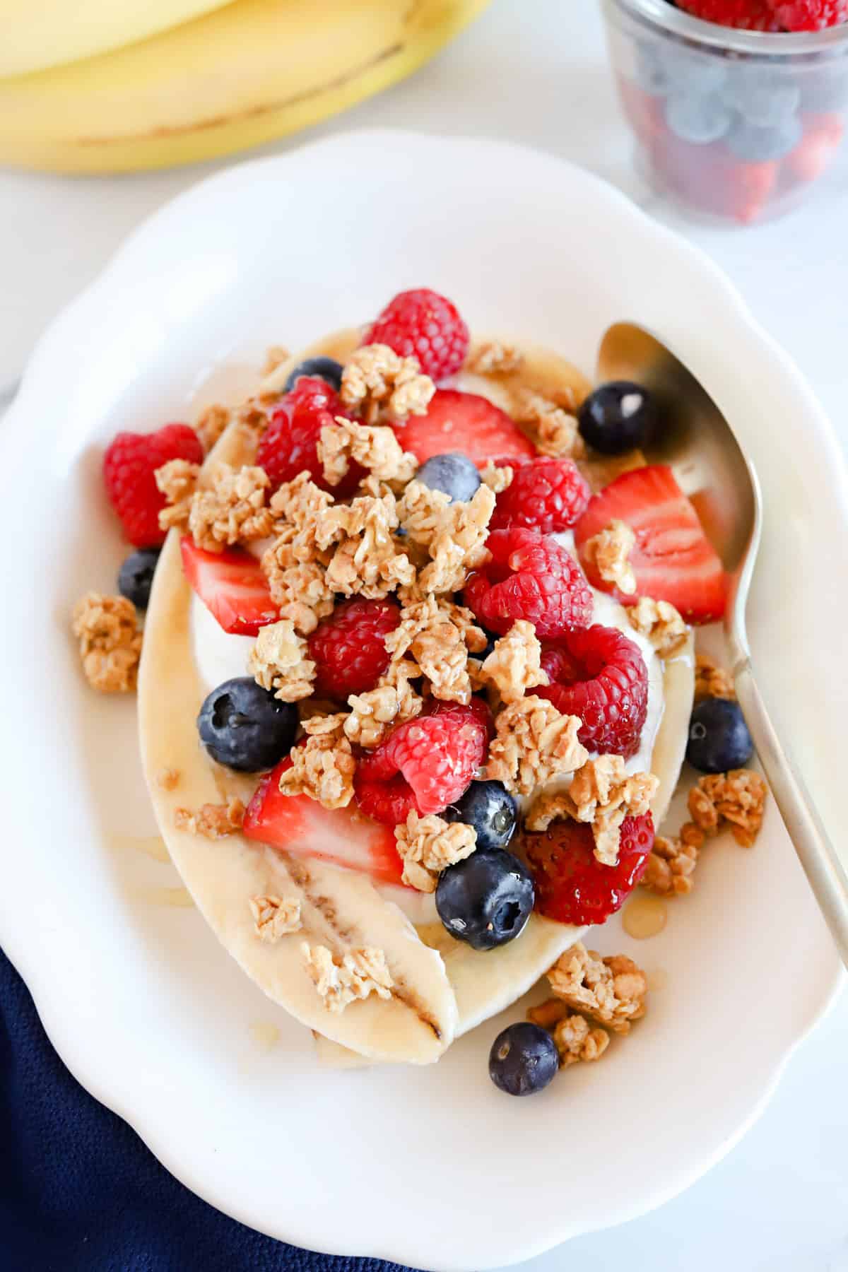 Breakfast banana split on a white plate with gold spoon.