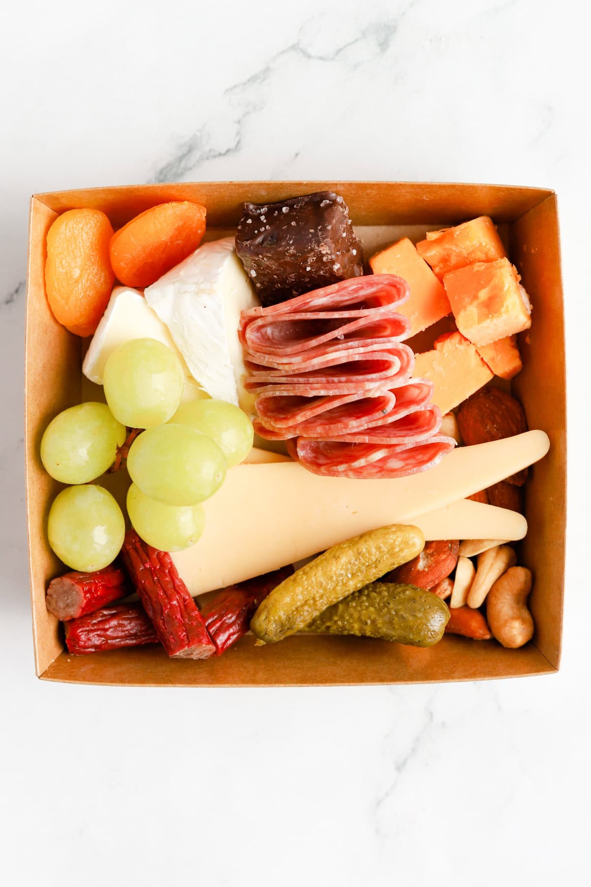 Charcuterie box filled with cheeses, meats, nuts, fruits, pickles and chocolate