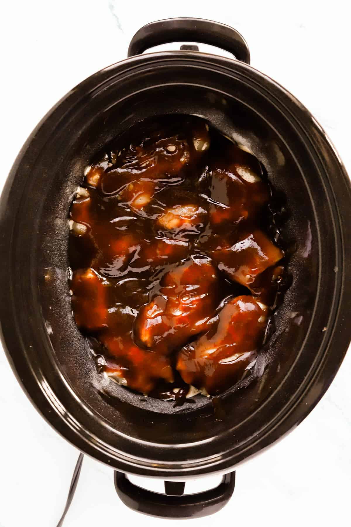 Chicken thighs in the bottom of the crockpot covered with barbecue sauce.