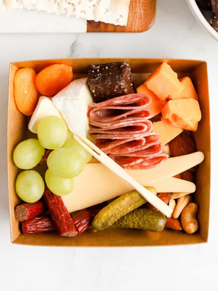 Charcuterie box filled with cheeses, meats, nuts, fruits, pickles and chocolate