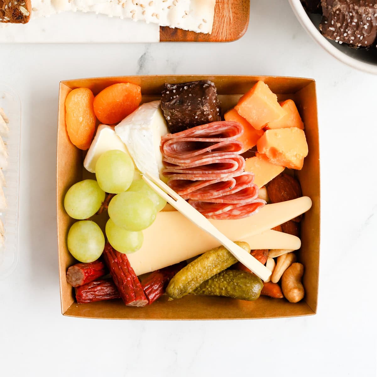 Charcuterie box filled with cheeses, meats, nuts, fruits, pickles and chocolate