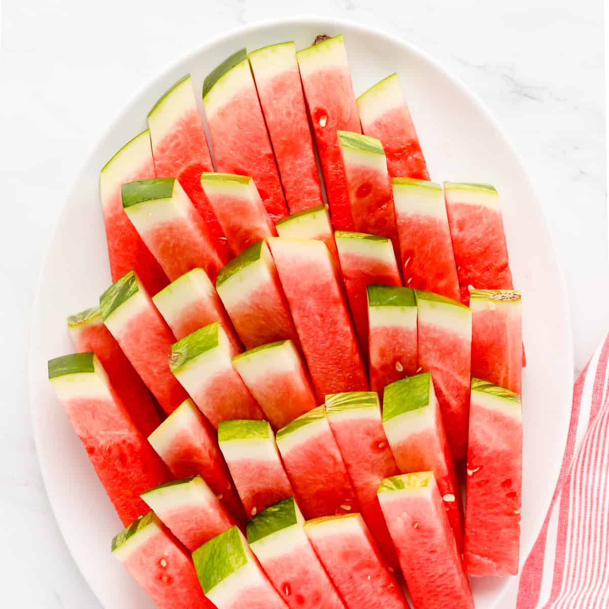 White oval platter of watermelon sticks.