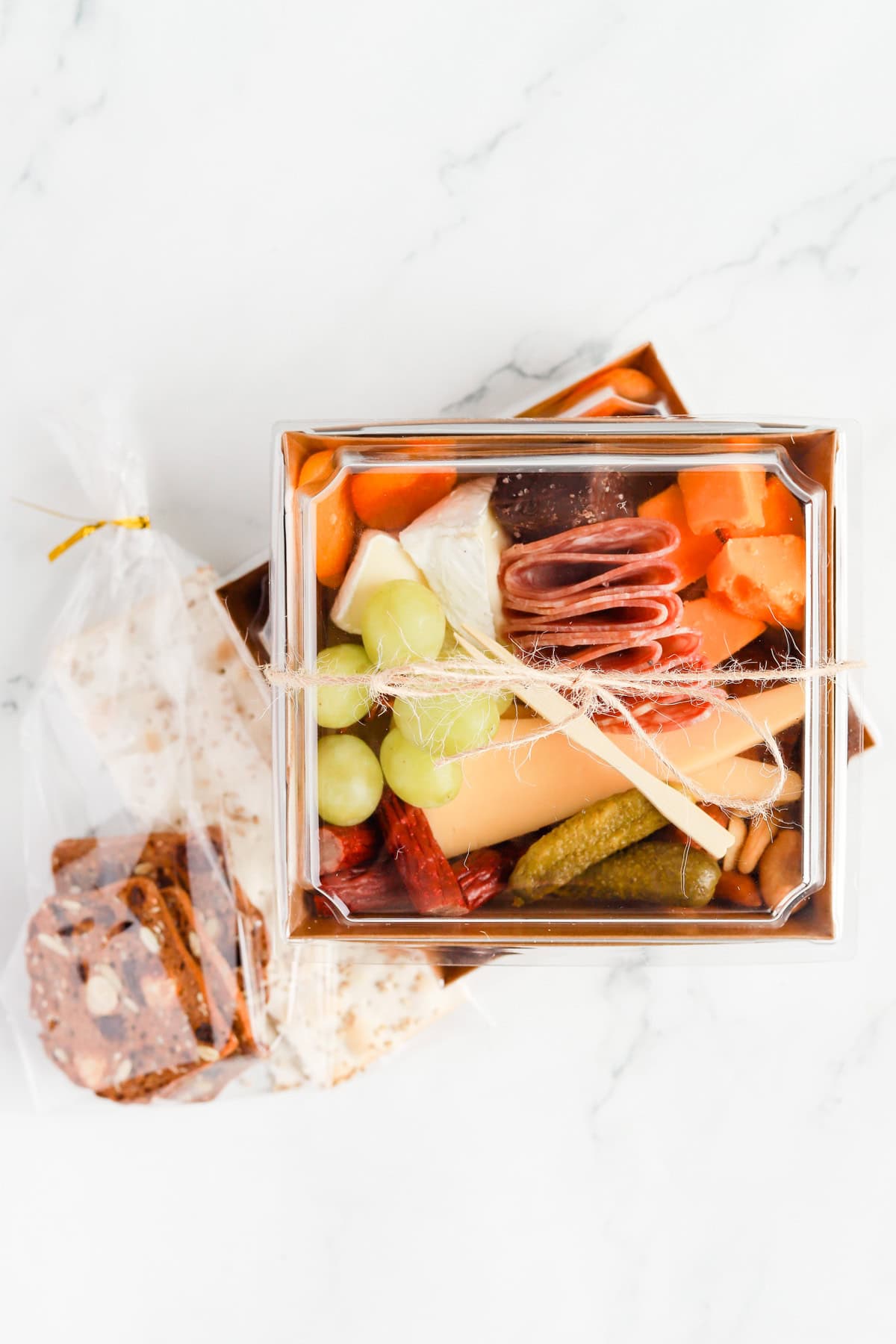 Packaged charcuterie boxes with crackers packaged in cellophane bags on the side.
