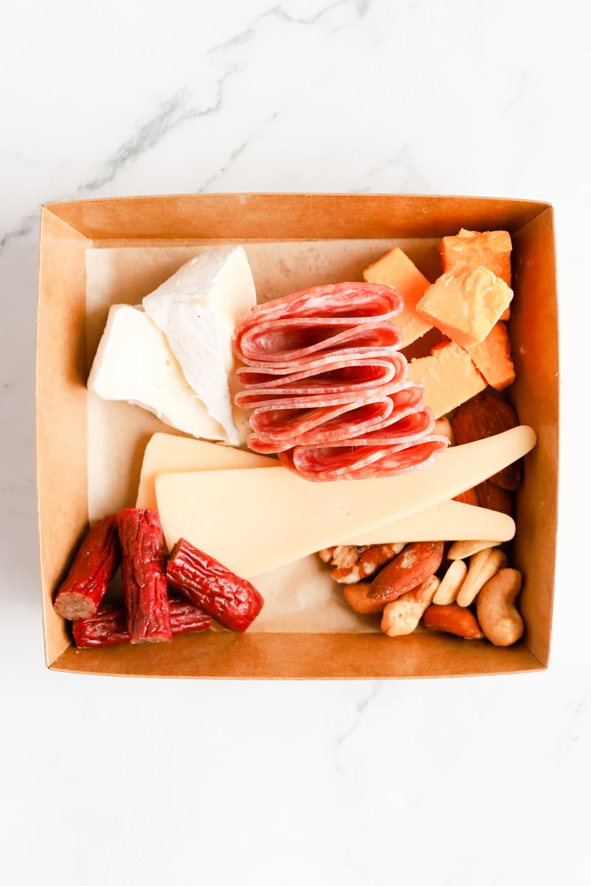 Sliced salami and cut meat sticks added to the box with cheese and nuts.