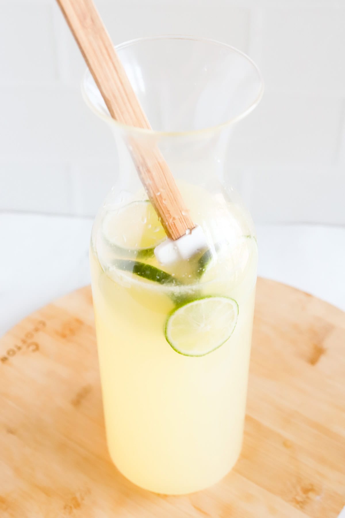 Rubber spatula stirring limeade in glass carafe.