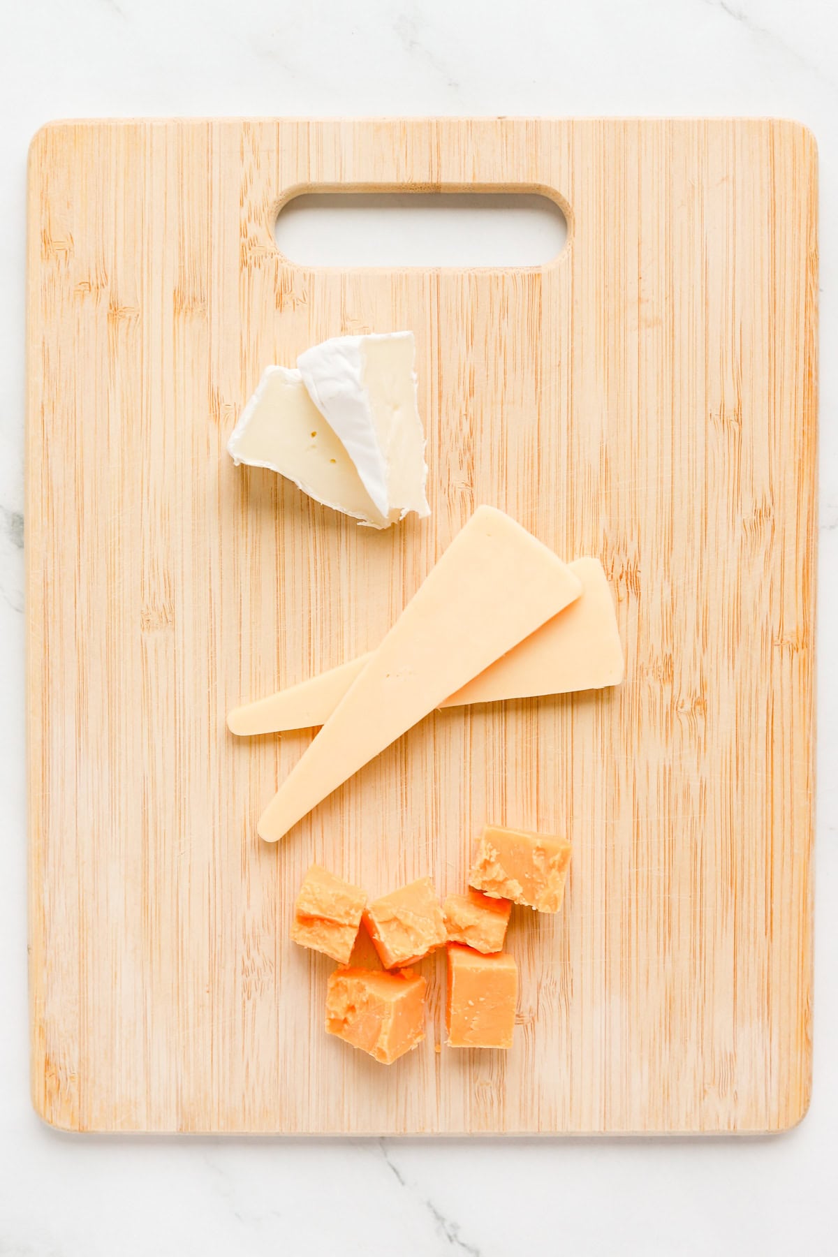 Small Brie wedges, edam cheese and sharp cheddar cheese on a wooden cutting board.