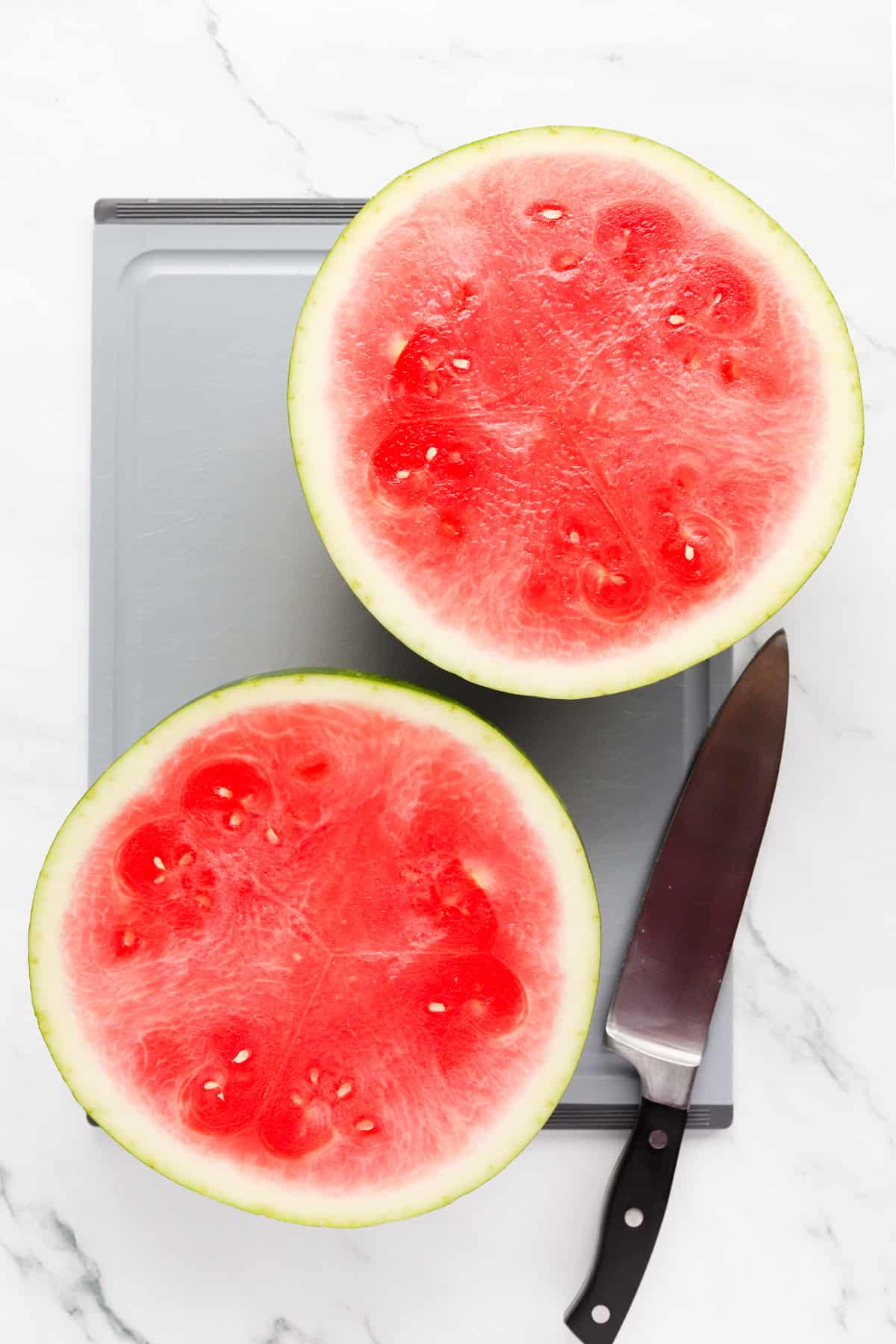 Watermelon sliced in half on a cutting board with a chef's knife