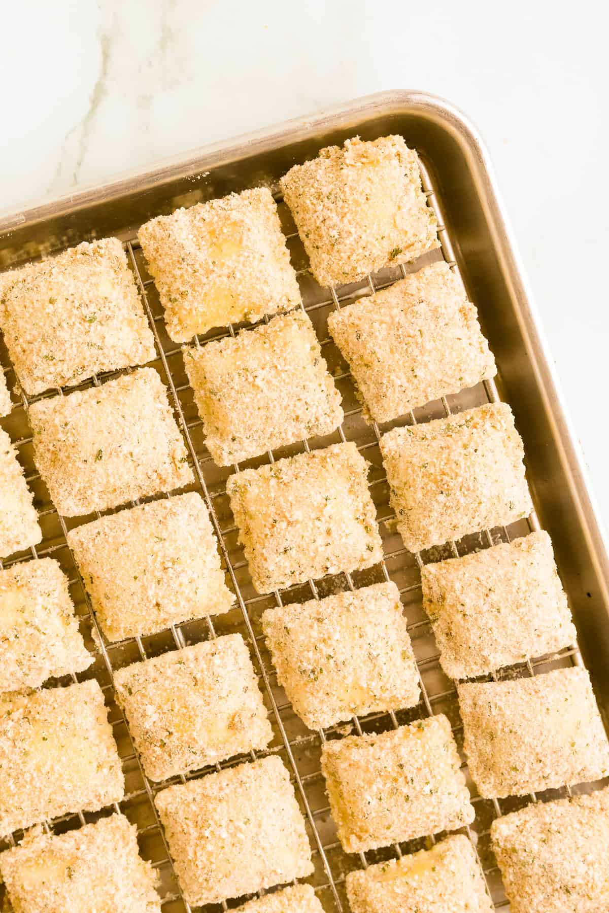 Breaded frozen ravioli on a wire rack on a baking sheet