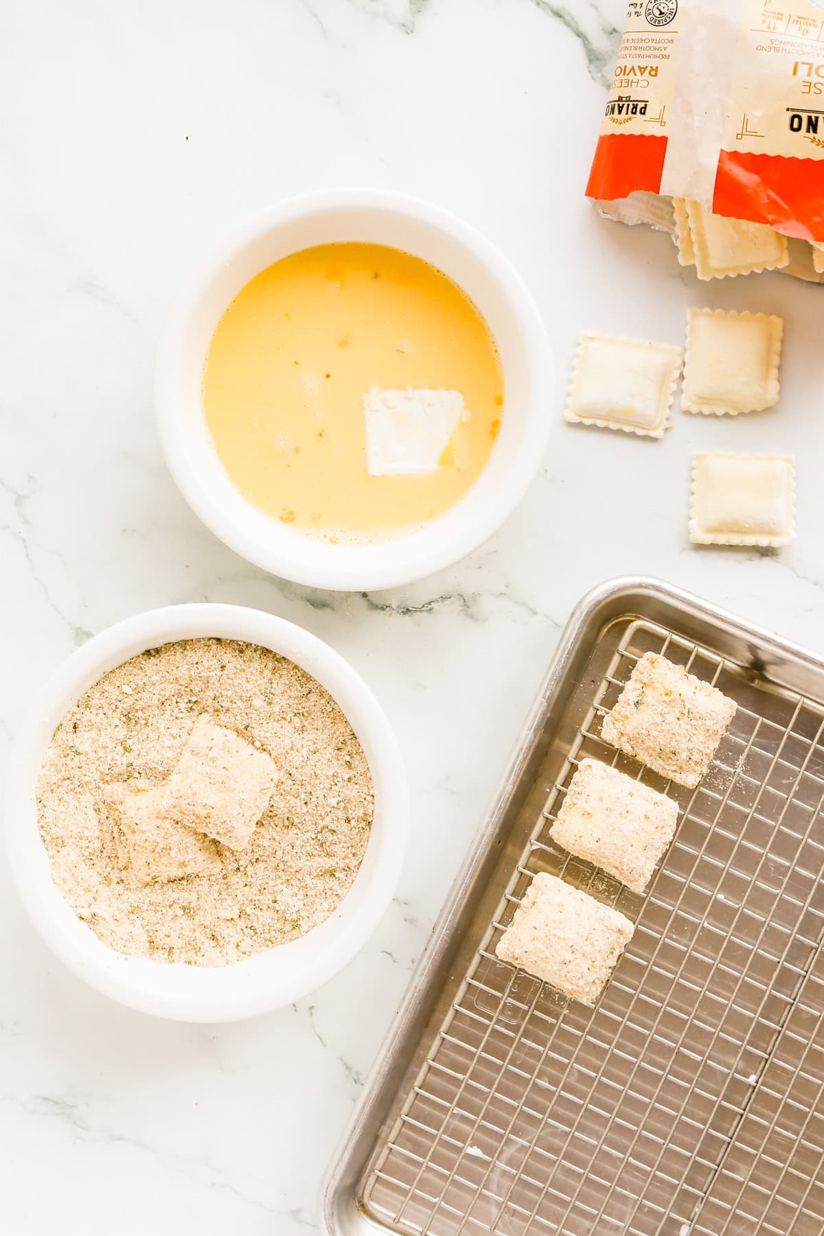 Dipping station for ravioli with a bowl of egg and milk, and another bowl of italian breadcrumbs and parmesan cheese.