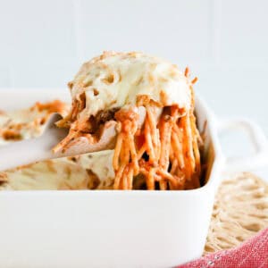 Featured image of a scoop of baked spaghetti casserole lifted out of white baking dish.