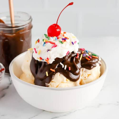 Featured image of a hot fudge sundae in a white bowl with rainbow sprinkles, whipped cream and a cherry on top.