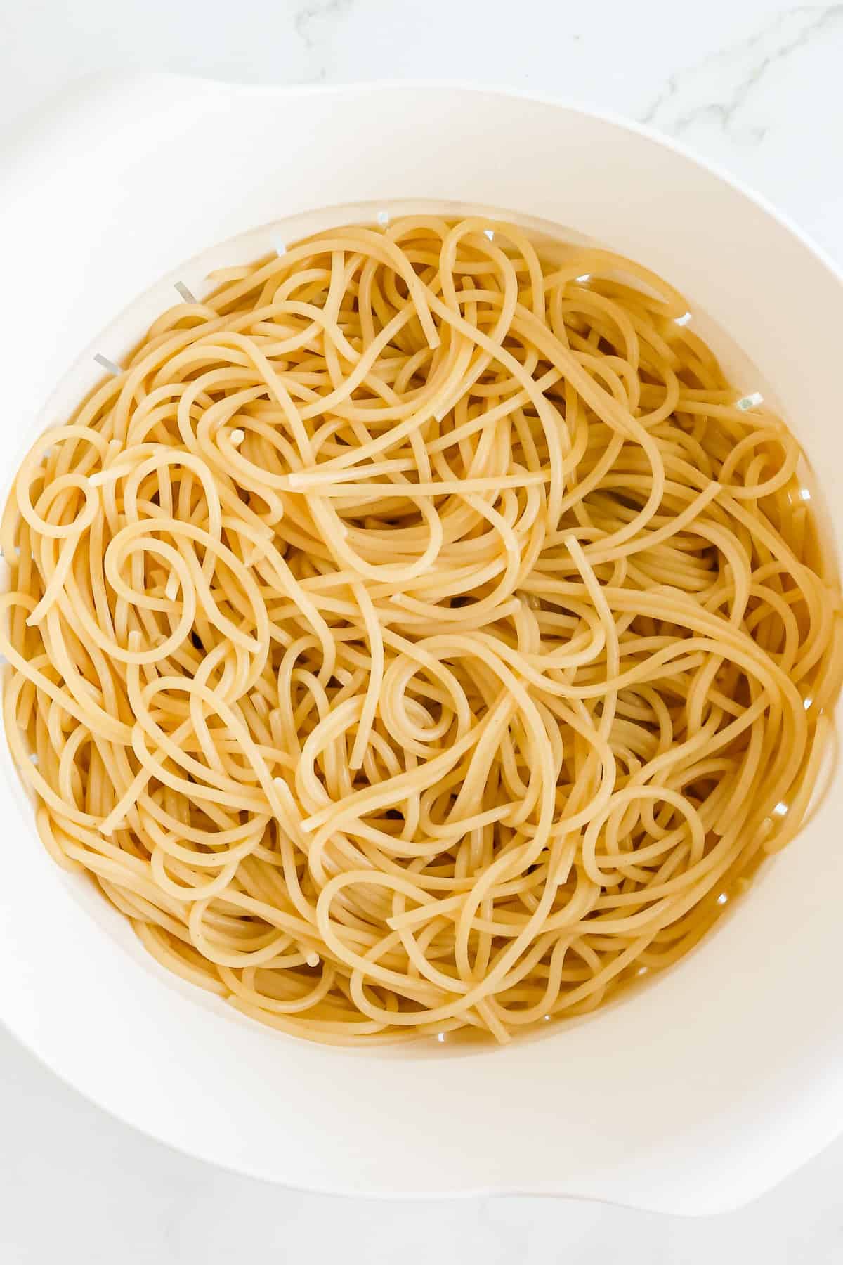 White colander of cooked spaghetti noodles