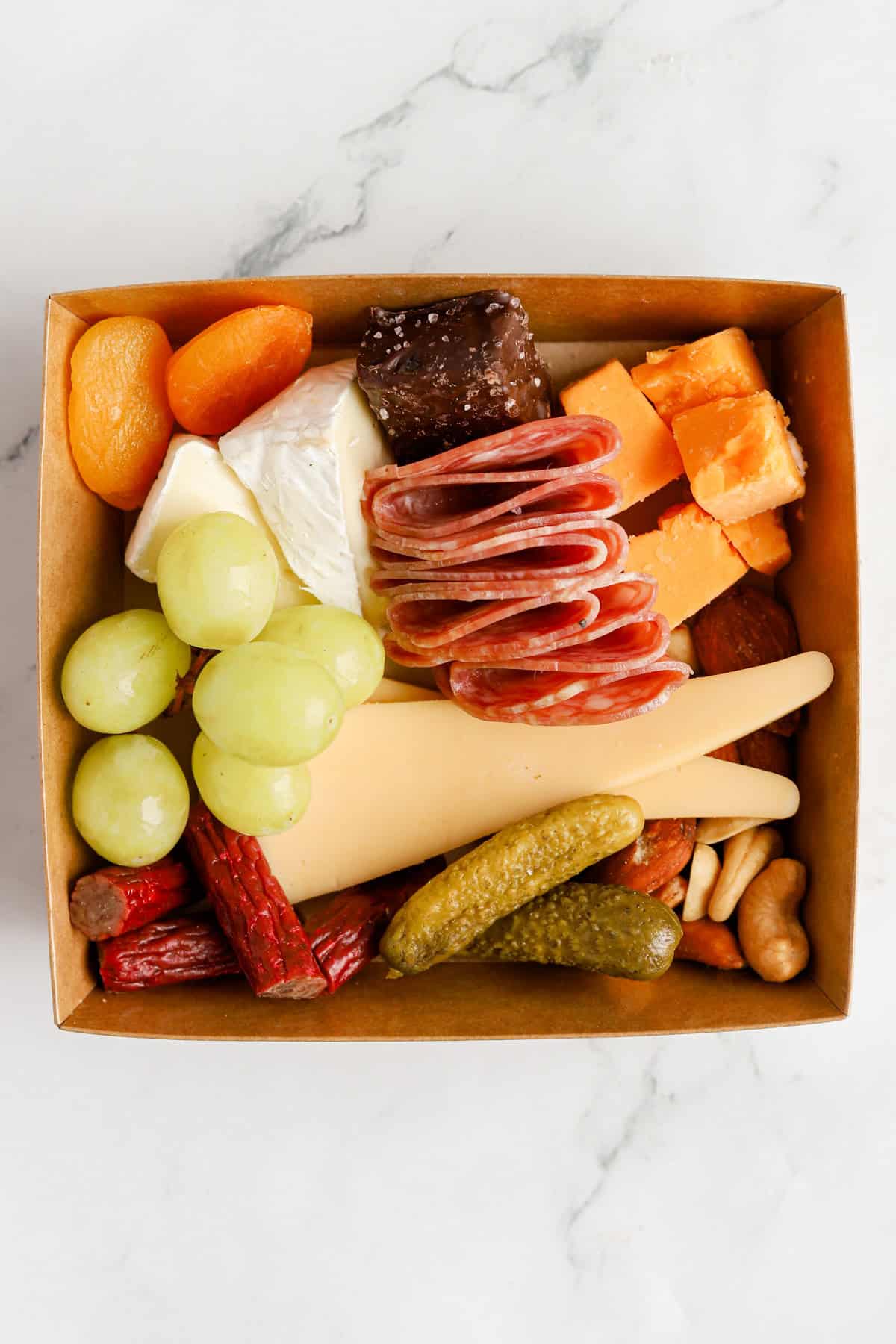 Charcuterie box filled with cheeses, meats, nuts, fruits, pickles and chocolate