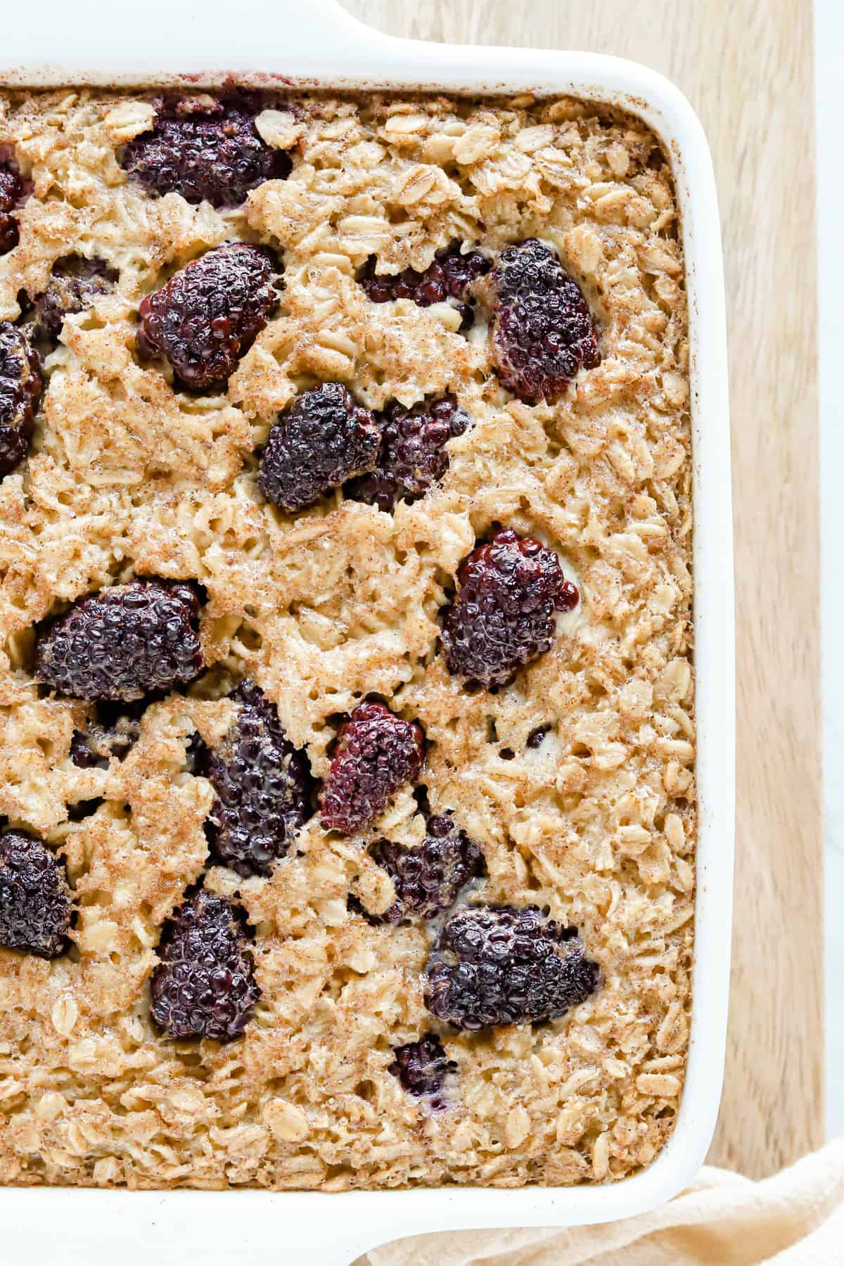 Overhead view of baked oatmeal in white baking dish with whole blackberries on top.