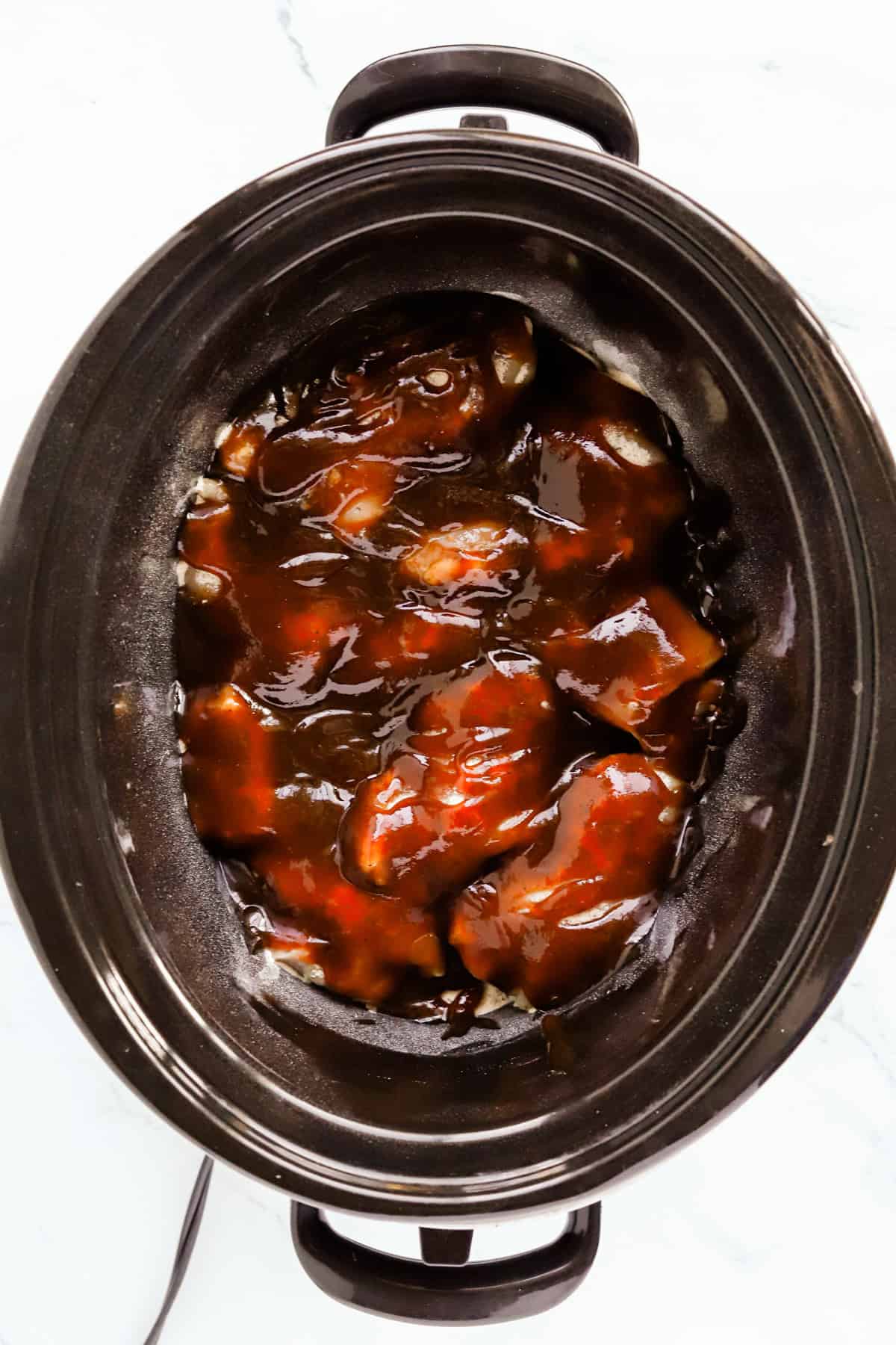 Chicken thighs in the bottom of the crockpot covered with barbecue sauce.