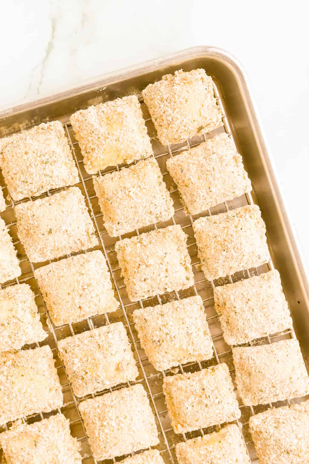 Breaded frozen ravioli on a wire rack on a baking sheet
