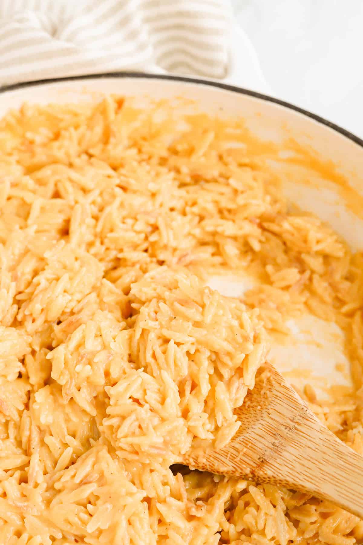Finished cheesy orzo in skillet with wooden spoon.