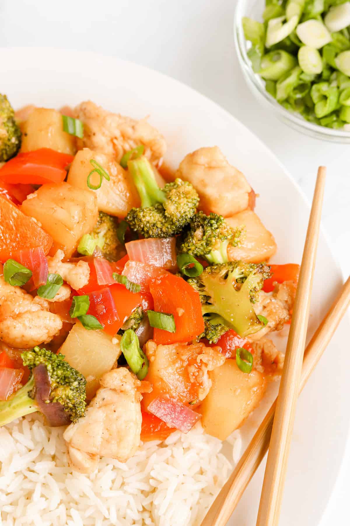 Close up of pineapple chicken stir fry on a white plate with chopsticks and green onions.