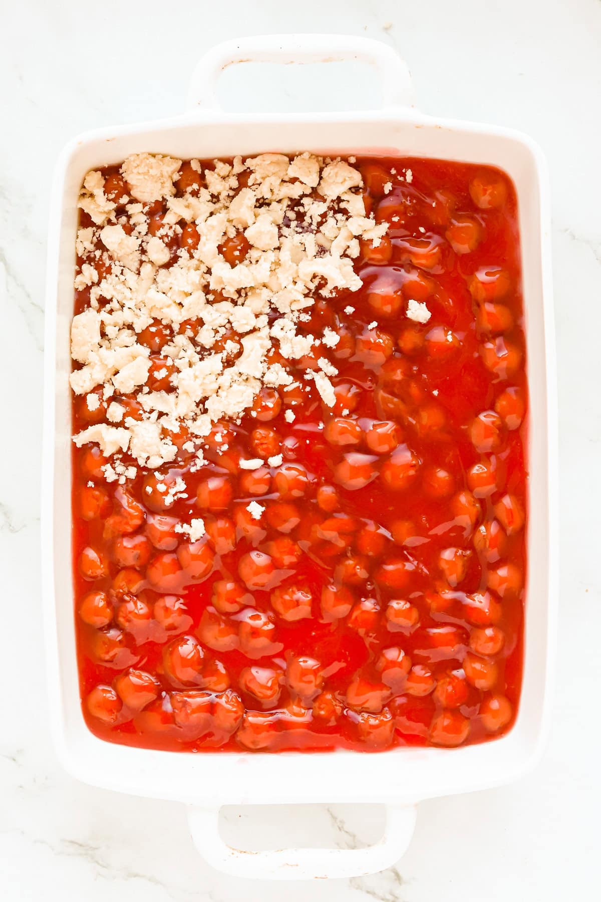 Cobbler topping partially covering pie filling in a white 9x13 baking dish