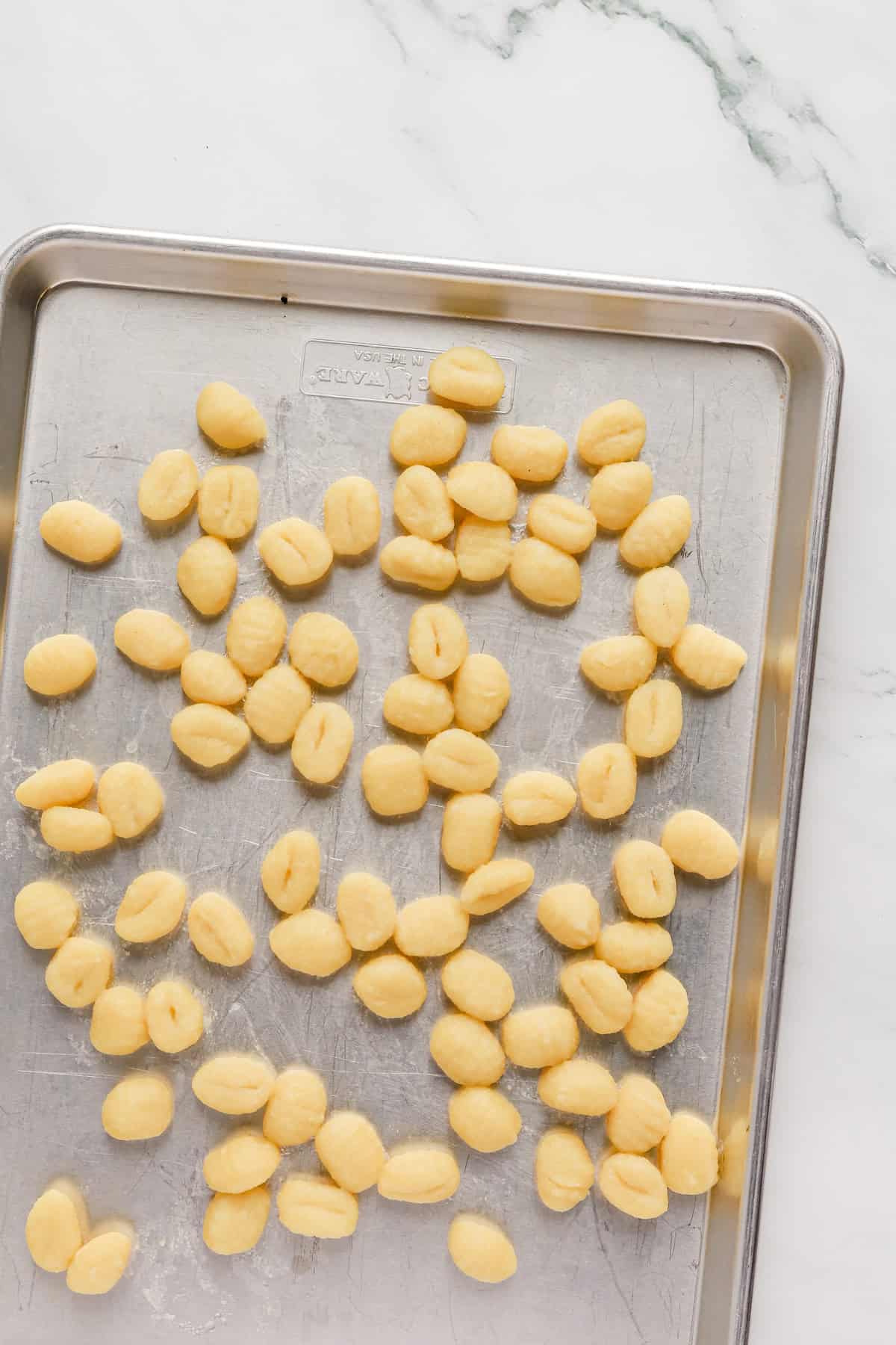 Cooked gnocchi cooling on a sheet pan.