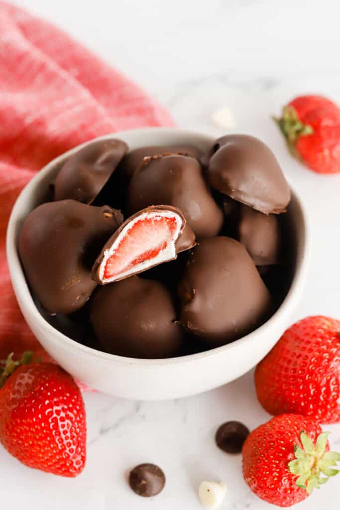 Small white bowl of dipped berries with one on top cut in half, exposing the center.