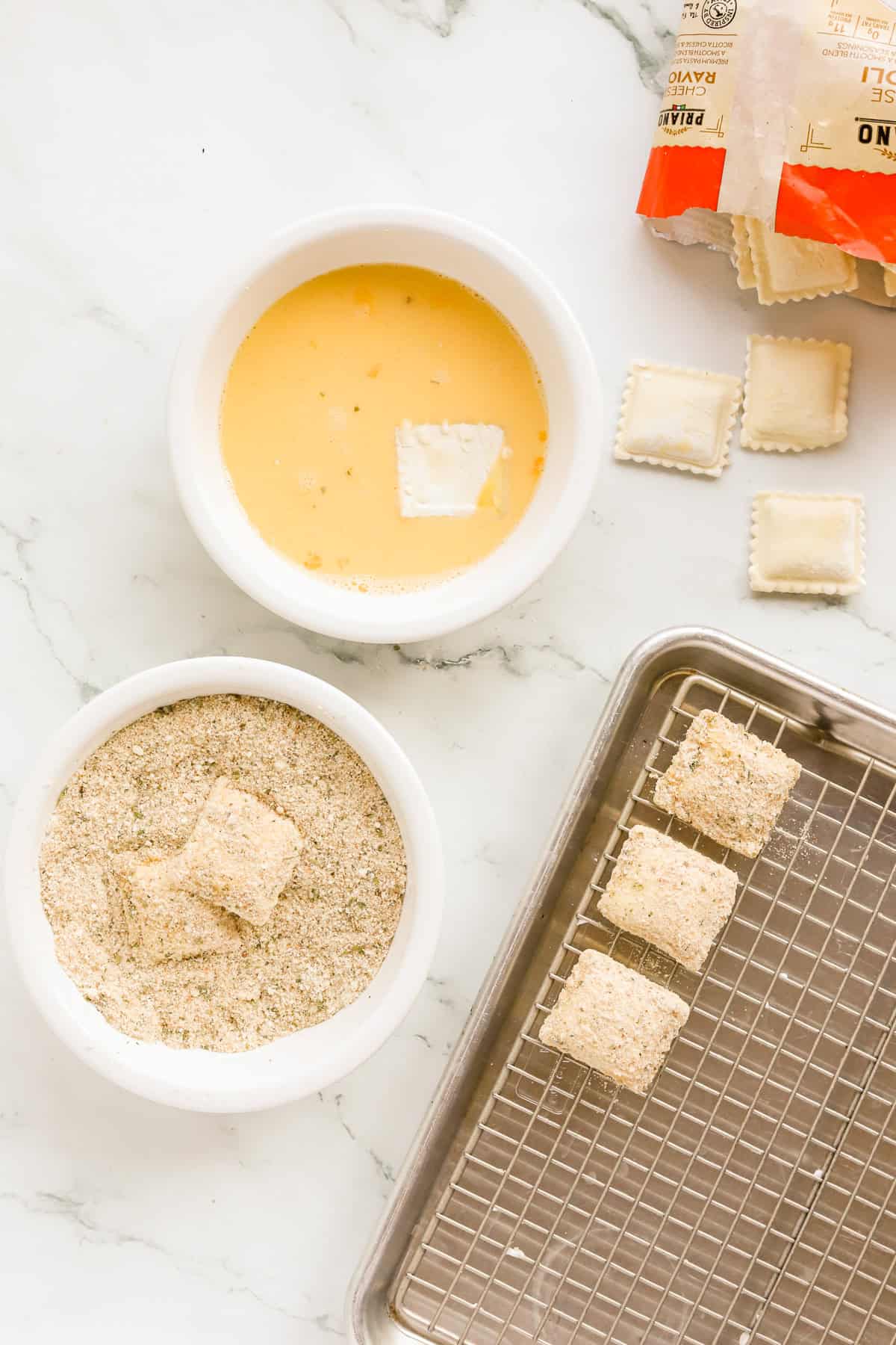 Dipping station for ravioli with a bowl of egg and milk, and another bowl of italian breadcrumbs and parmesan cheese.