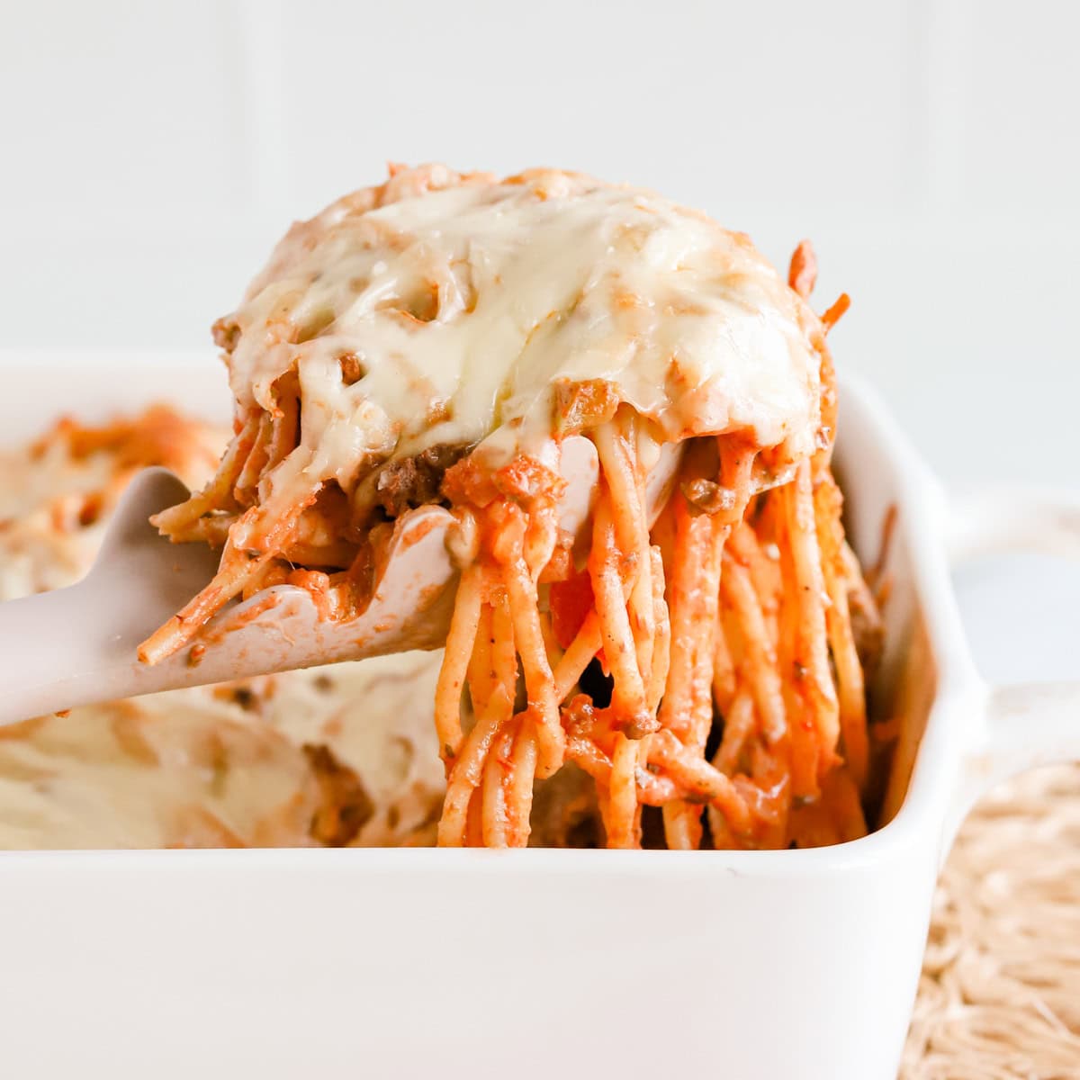 Featured image of a scoop of baked spaghetti casserole lifted out of white baking dish.